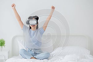 Young asian woman wearing vr headset playing game with excited in the bedroom at home.
