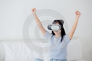 Young asian woman wearing vr headset playing game with excited in the bedroom at home.