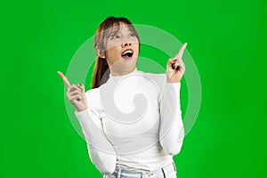 Young Asian woman wearing white shirt pointing at something on green screen