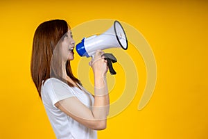 Young Asian woman in white casual t-shirt looking aside, scream in megaphone isolated on bright yellow
