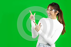 Young asian woman in white shirt wearing glasses pointing fingers on copy space, Virtual Reality concept greenscreen