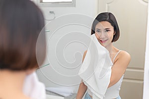 Young asian woman wiping her face with towel in bathroom