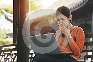 Young asian woman working with her laptop and she feel worried in the park outdoors on vacation time