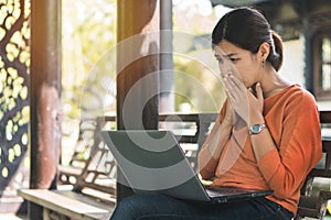 Young asian woman working with her laptop and she feel worried in the park outdoors on vacation time