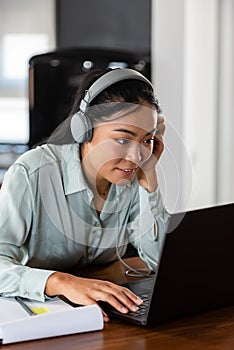 Young Asian woman working from home. Sitting in front of laptop computer with headphones, having online meeting