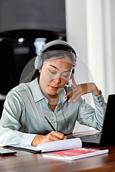 Young Asian woman working from home. Sitting in front of laptop computer with headphones, having online meeting