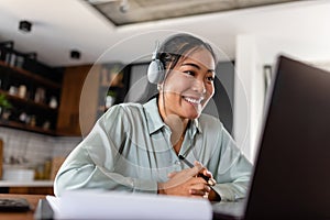 Young Asian woman working from home. Sitting in front of laptop computer with headphones, having online meeting