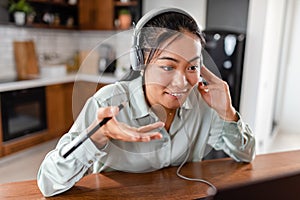 Young Asian woman working from home. Sitting in front of laptop computer with headphones, having online meeting