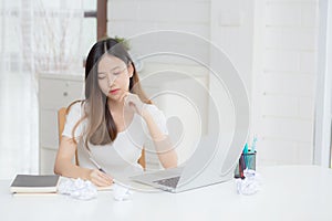 Young asian woman working with laptop computer think idea project and paper crumpled having problem on table.