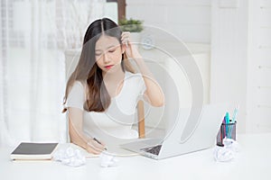 Young asian woman working with laptop computer think idea project and paper crumpled having problem on table at home.