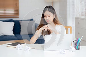 Young asian woman working with laptop computer think idea project and paper crumpled having problem on table at home girl using