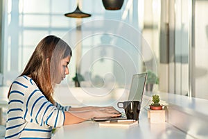 Young asian woman working on a laptop with drinking coffee and sit at home office