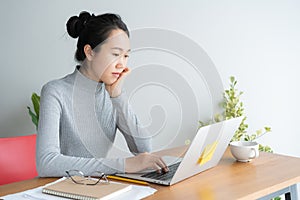 Young asian woman working on laptop in the home office desk, And sit at table resting chin on hand