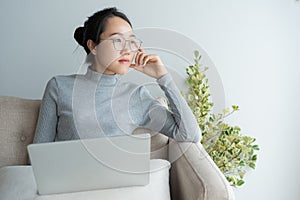 Young asian woman working on laptop in the home  And sit at sofa resting chin on hand.