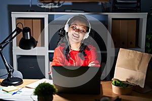 Young asian woman working at the office with laptop at night happy face smiling with crossed arms looking at the camera