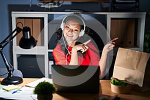 Young asian woman working at the office with laptop at night smiling and looking at the camera pointing with two hands and fingers