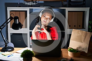 Young asian woman working at the office with laptop at night smiling in love doing heart symbol shape with hands