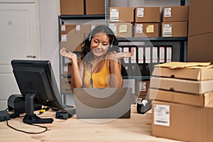 Young asian woman working at small business ecommerce wearing headset clueless and confused expression with arms and hands raised