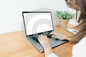 Young Asian woman working using and typing on laptop with mock up blank white screen while at home in office work space.