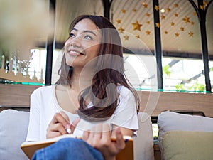 Young Asian woman or a writer sitting in a journal or writing a novel in a coffee shop outside the office. Freelance women are rel