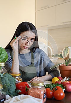 Young Asian woman writes down recipe for a dish in notebook. Zero waste. Vegetarian woman