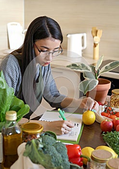 Young Asian woman writes down recipe for a dish in notebook. Zero waste. Vegetarian woman