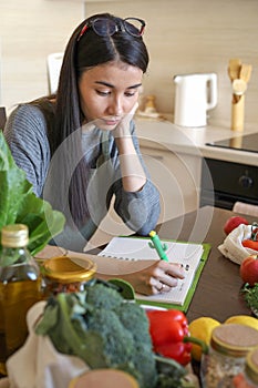 Young Asian woman writes down recipe for a dish in notebook. Zero waste. Vegetarian woman