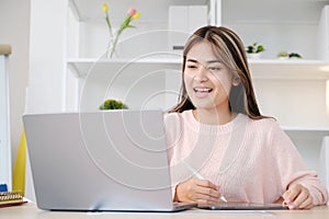 Young asian woman writing on digital tablet while make video conference by laptop computer