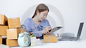 Young Asian woman is writing down the customer`s details and addresses on the mailbox in order to prepare for shipping