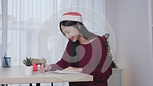 Young asian woman writing postcard in Christmas day at home, eve and celebrate, female writing message on greeting card.