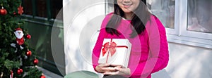 Young Asian women holding white gift box smiling and happy with Christmas decoration on the background