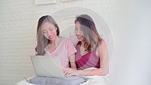Young Asian women lesbian happy couple using computer laptop checking social media in bedroom at home.