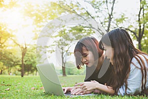 Young asian women lying on grass and using laptop and typing. Girls hands on keyboard.