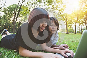 Young asian women lying on grass and using laptop and typing. Girls hands on keyboard.