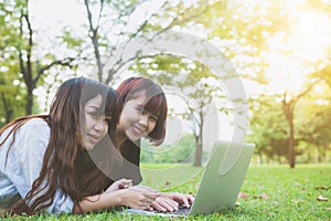 Young asian women lying on grass and using laptop and typing. Girls hands on keyboard.