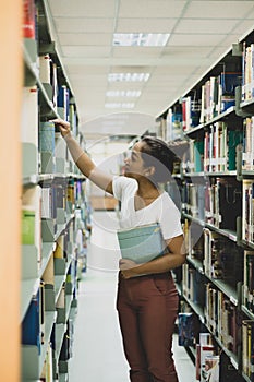 Young Asian women are searching for books and reading from the bookshelves in the college library to research and develop