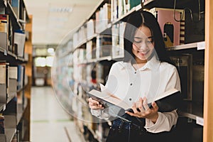 Young Asian women are searching for books and reading from the bookshelves in the college library to research and develop