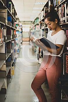 Young Asian women are searching for books and reading from the bookshelves in the college library to research and develop