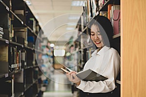 Young Asian women are searching for books and reading from the bookshelves in the college library to research and develop