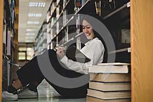 Young Asian women are searching for books and reading from the bookshelves in the college library to research and develop