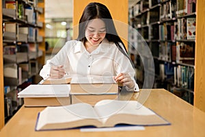 Young Asian women are searching for books and reading from the bookshelves in the college library to research and develop