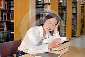 Young Asian women are searching for books and reading from the bookshelves in the college library to research and develop