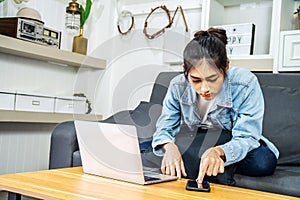 Young Asian women sit on the sofa to work at home. Looking for information on laptops and mobile phones to get the job done