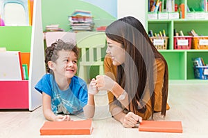 Young asian woman teacher teaching american kid in kindergarten classroom with happiness and relaxation.