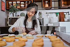 Young Asian women wearing aprons and gloves while decorating various donuts with layers of chocolate