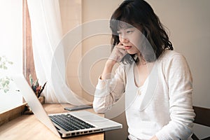 Young Asian worker woman working with laptop computer. A woman thinking of some idea and feeling stress while working from home.