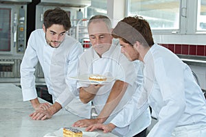 Young assistants and mature chef looking at finished cake