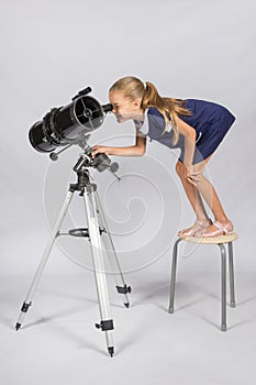 The young astronomer standing on a chair and funny looking in a telescope eyepiece