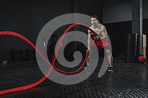 Young athlete doing battle ropes exercise at the crossfit gym