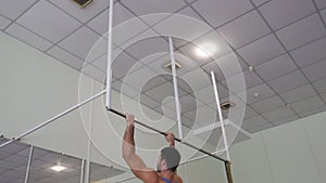 Young athlete doing hard exercises on horizontal bar at gym. Strong gymnast doing pull ups during workout. Muscular